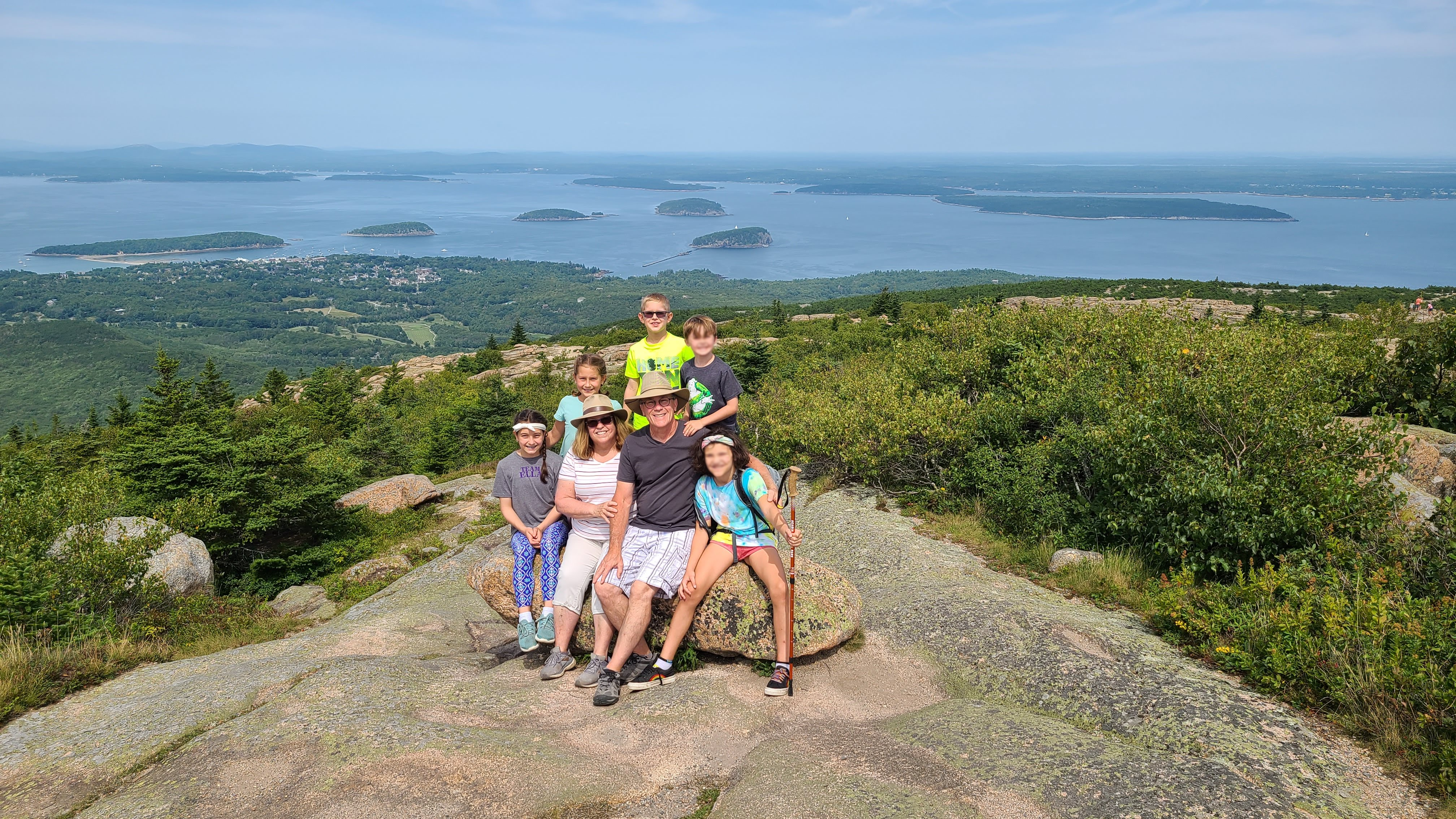 Family of 7 posing on top of large stone at top of a mountain