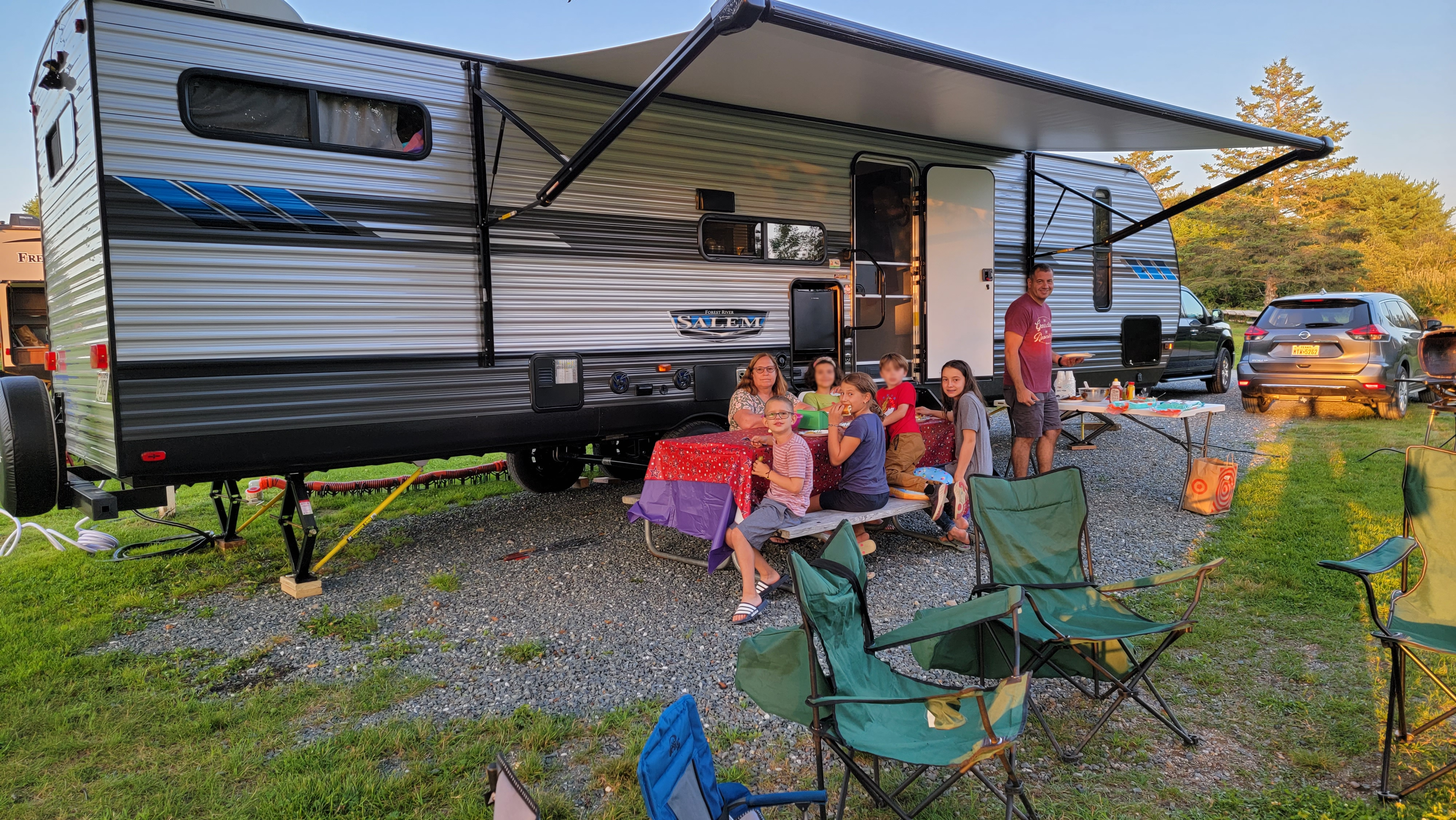 Family of 7 eating at picnic table in front of travel trailer
